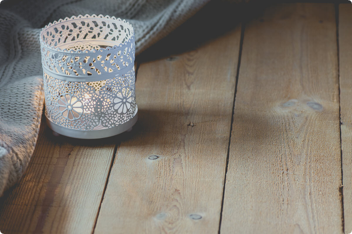 Lit candle beside a soft blanket on a wooden table Lit candle beside a soft blanket on a wooden table